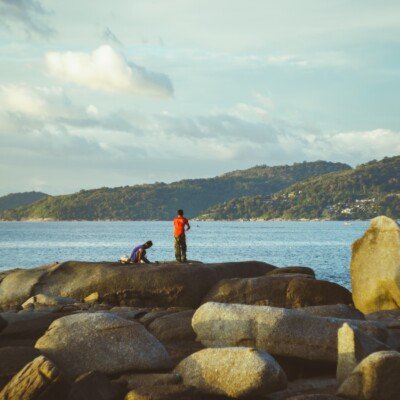 two people standing on rocks near the ocean