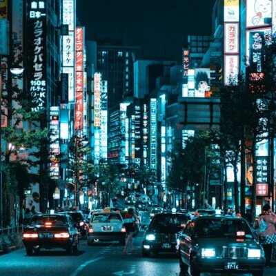 vehicles on roadway between lighted buildings at night